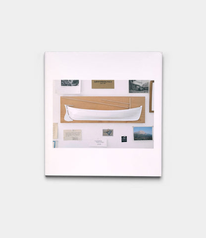 The "Boats, Books, Birds" by Best Made Co. is a framed display with a white hand-carved wooden boat on beige, artfully surrounded by photos, postcards, and documents.