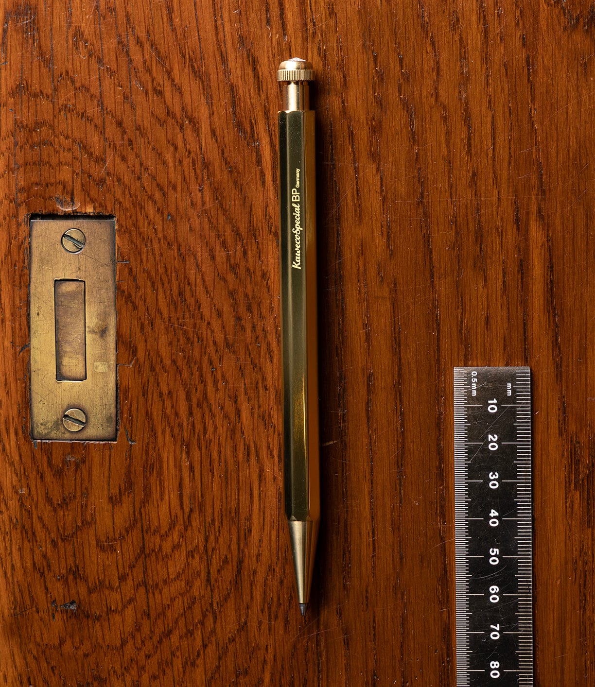 The Best Made Co. Kaweco Special, a gold octagonal mechanical pencil, rests on a wooden surface beside a metal ruler marked in centimeters and millimeters, and a brass latch plate.