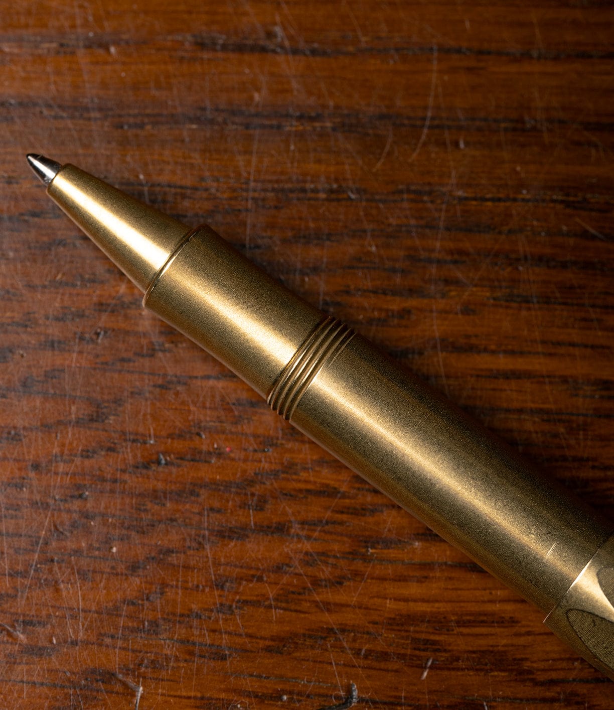 A close-up of the Best Made Co. Kaweco Sport brass pocket pen, compatible with a G2 rollerball refill, resting on a scratched, grainy wooden surface.