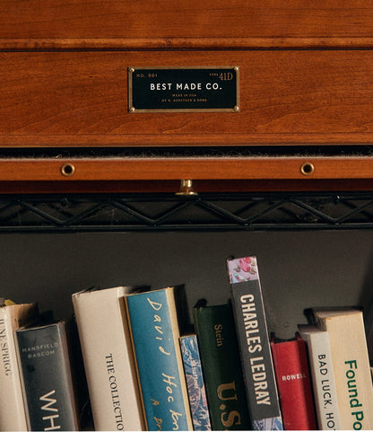 A close-up of a bookshelf featuring an array of books with a wooden Gerstner 41D Founder’s Edition drawer above, echoing the design of classic chests, and the Best Made Co. label visible at the top of the image.
