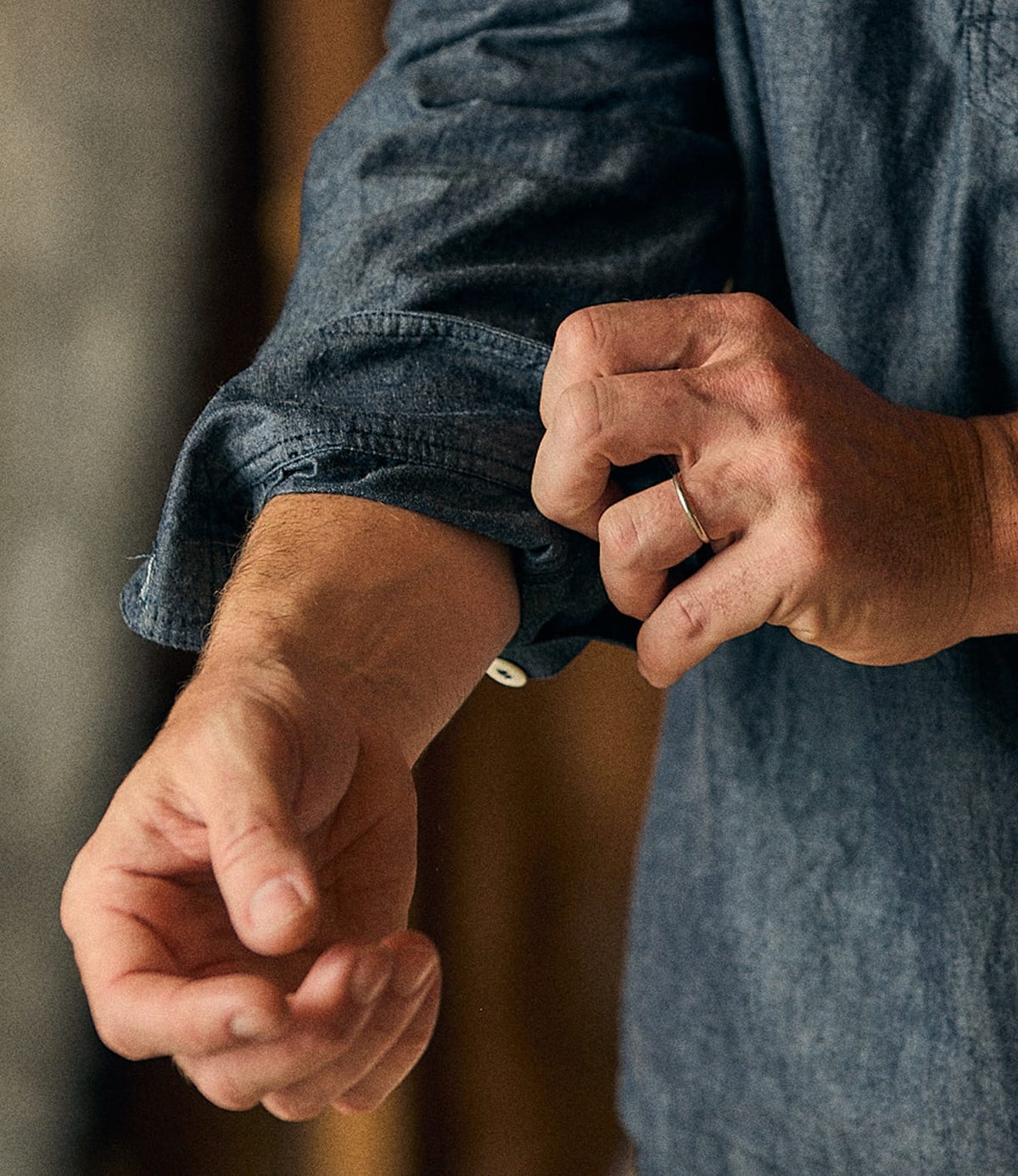 A person wearing the Best Made Co. Indigo Chambray Popover rolls up their sleeve.