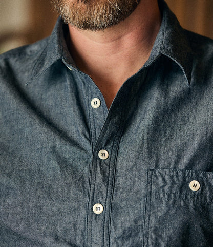 Close-up of a person wearing the Best Made Co. Indigo Chambray Popover, a blue button-up shirt made from premium Fukuyama woven cotton with white buttons and a front pocket. The wearer’s beard and part of their neck are visible.