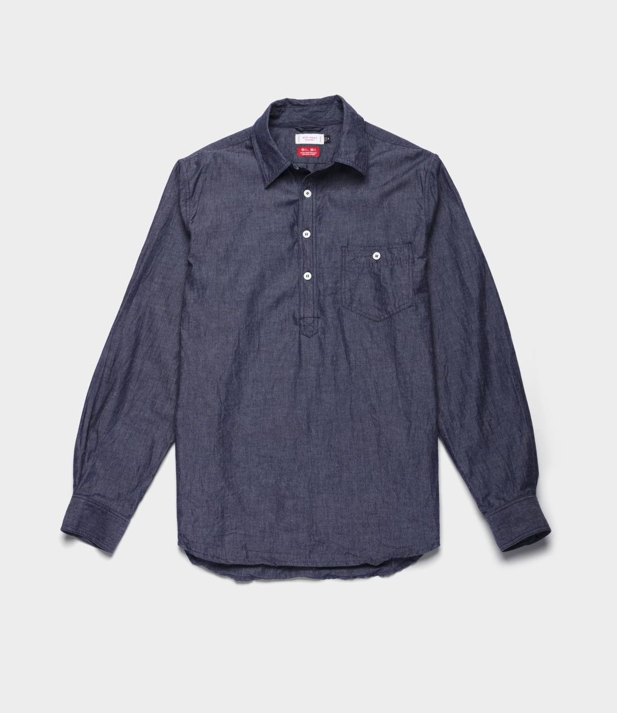 The Best Made Co. Indigo Chambray Popover is a long-sleeve, dark blue chambray woven shirt featuring a partial button placket, single chest pocket, and buttoned cuffs, shown laid flat on a light background.
