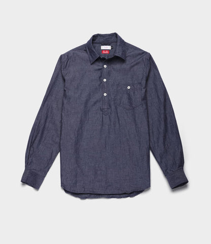 The Best Made Co. Indigo Chambray Popover is a long-sleeve, dark blue chambray woven shirt featuring a partial button placket, single chest pocket, and buttoned cuffs, shown laid flat on a light background.