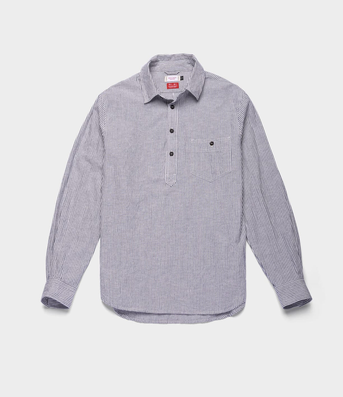 The Indigo Stripe Popover by Best Made Co. is a long-sleeve, button-up shirt with thin black and white vertical stripes, expertly crafted from premium Japanese cotton-linen. Featuring a classic collar and a front pocket on the left chest, this versatile year-round shirt is displayed laid flat against a plain white background.