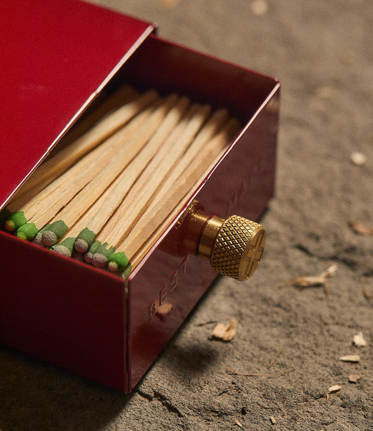 Best Made Co. Sliding Match Safe Red, partially open to reveal a row of strike-anywhere matches with green tips, featuring a textured brass knob on a red metal sliding case.