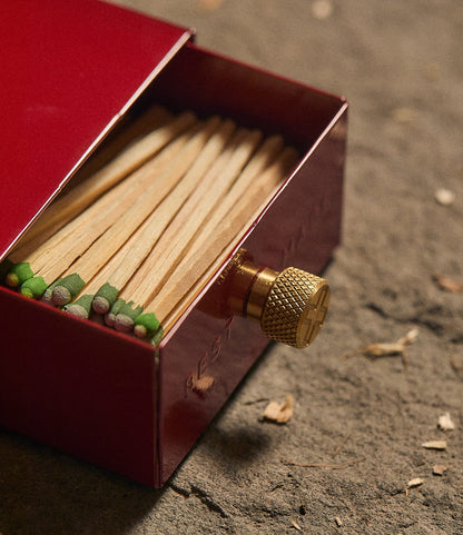 Best Made Co. Sliding Match Safe Red, partially open to reveal a row of strike-anywhere matches with green tips, featuring a textured brass knob on a red metal sliding case.