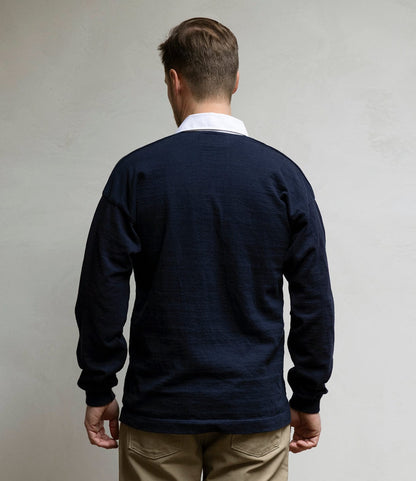 A man with short brown hair, seen from behind, wears the Best Made Co. McArthur Rugby Jersey in navy with a white collar and beige pants against a light gray background.