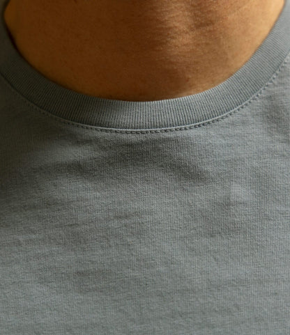 Close-up of a person's neck and upper chest wearing the Best Made Co. Standard T-Shirt in Overcast Blue, highlighting the garment-dyed premium cotton fabric texture and collar stitching detail.