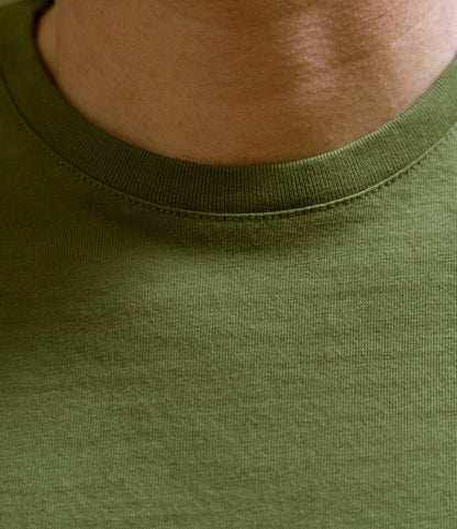A close-up of a person's neck and upper chest wearing the Best Made Co. Standard T-Shirt in Olive Drab, highlighting the soft Peruvian tangüis cotton fabric texture and durable crew neck design.