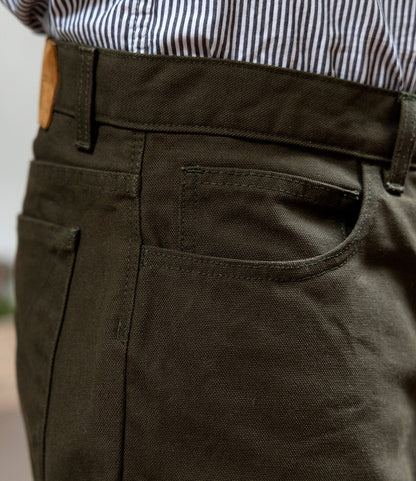 Close-up of a person wearing Best Made Co.'s Standard 5-Pocket Pant in Deep Olive, styled with visible front and coin pockets and paired with a white and blue vertically striped shirt for a classic straight leg look.