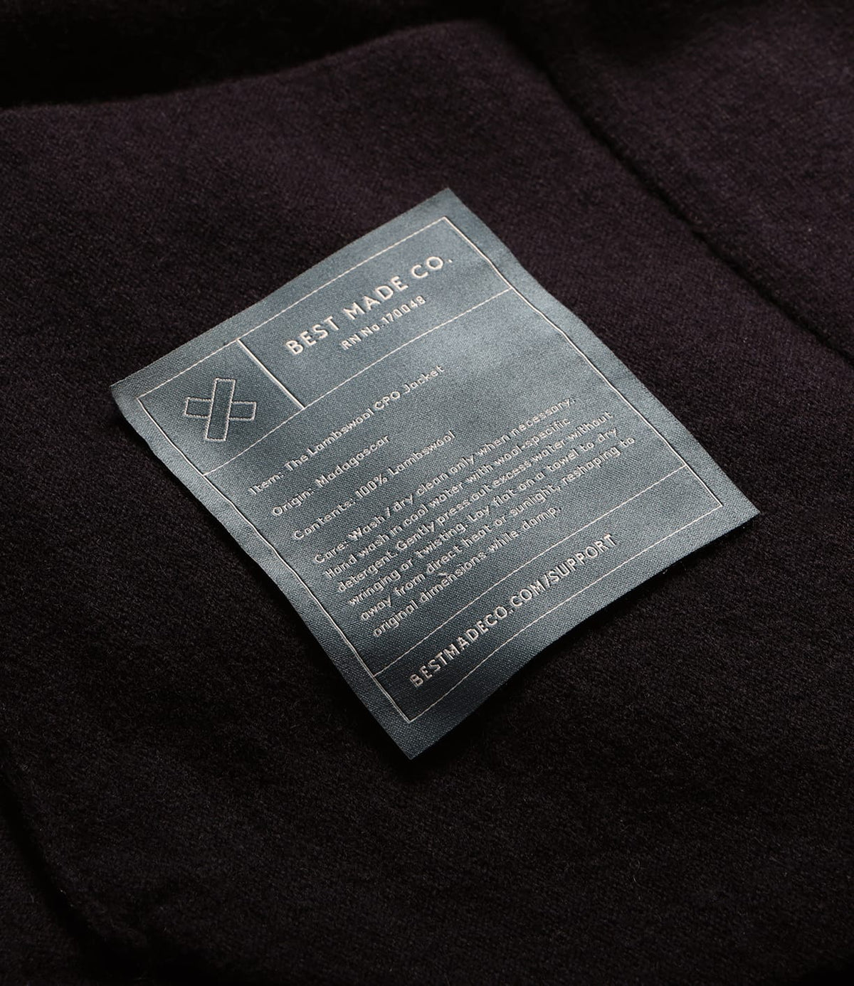 A rectangular clothing label sewn onto a dark Knit Lambswool CPO shirt, listing care instructions, fiber content, and origin information.