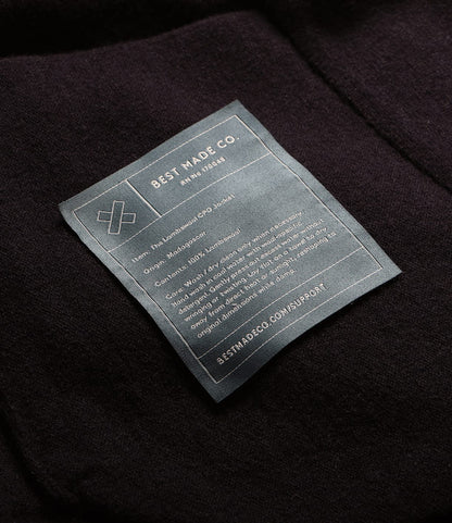 A rectangular clothing label sewn onto a dark Knit Lambswool CPO shirt, listing care instructions, fiber content, and origin information.