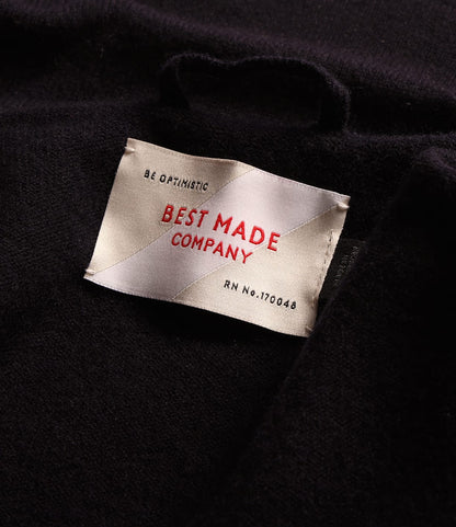 Close-up of a clothing label on a dark merino wool Knit Lambswool CPO shirt, reading Be Optimistic, Best Made Company, and RN No. 170048.