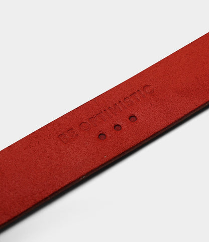 A close-up of Best Made Co.'s Famous Red Belt, made in the USA, features "BE OPTIMISTIC" embossed on red leather and three small circular holes below the text.
