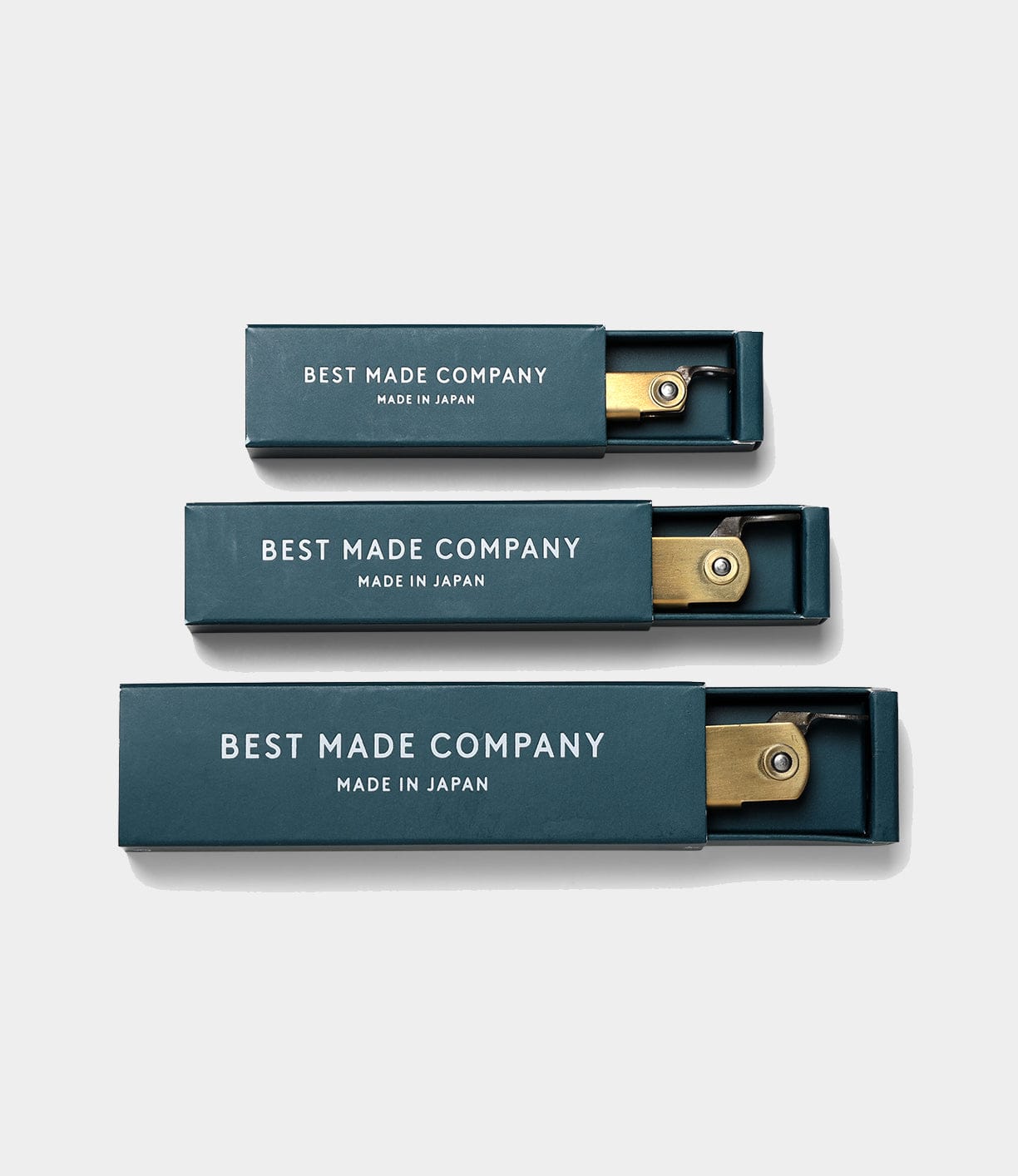 Three blue rectangular boxes labeled Best Made Co and MADE IN JAPAN each hold a partially visible Max Brass Higo Knife, a Japanese folding knife, arranged from smallest to largest on a white background.