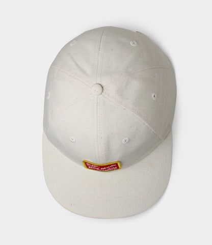 The Best Made Co. Selvedge Natural Denim Ball Cap seen from above showcases a white denim design with a small rectangular red and yellow patch on the front.