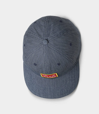 The Best Made Co. Small Stripe Indigo Ball Cap features blue pinstripes and a small yellow-and-red rectangular patch on the front, shown from above on a plain light background.