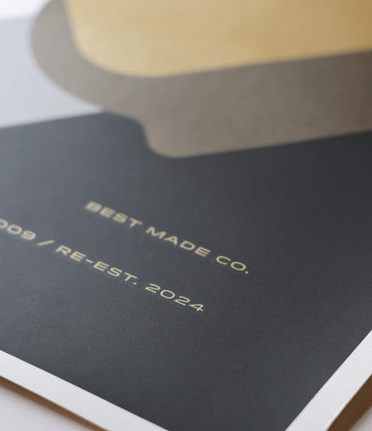 A close-up of the “Good as Gold” Silk-Screened Poster by Best Made Co., showing abstract beige and gray shapes by Jason Munn and light gold lettering: BEST MADE CO. and 2009 / RE-EST. 2024 on a dark background above limited edition text.