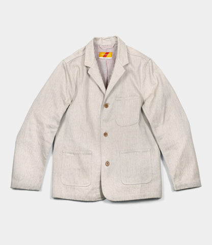 The Best Made Co. Selvedge Natural Studio Jacket features light beige selvedge fabric, three buttons, two large front pockets, a chest pocket, and striped collar lining—shown flat on white to highlight classic American craftsmanship.