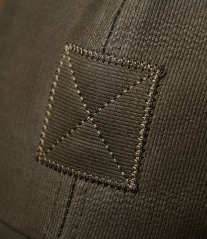 Close-up of olive drab fabric with visible stitching, featuring a square patch with an “X” pattern—showcasing the durable craftsmanship of the Best Made Co. Military Cord Ball Cap Olive Drab.