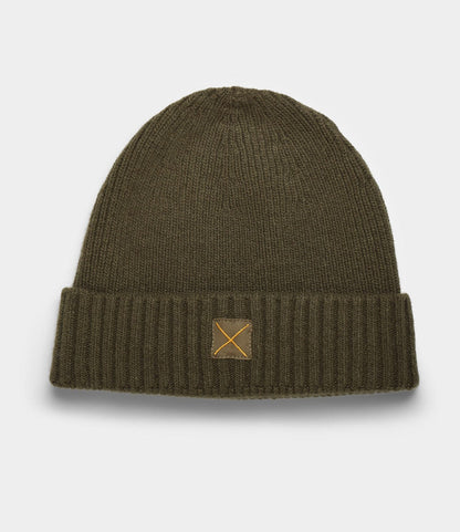 The Cap of Courage by Best Made Co. is a dark olive green lambswool cap with a folded cuff, featuring a small tan patch with a stitched X at the front center, shown on a plain light background.