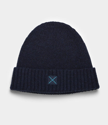 The Cap of Courage by Best Made Co. is a navy blue lambswool knit beanie with a folded brim and a small square patch featuring a light blue X on the front, shown against a plain white background.