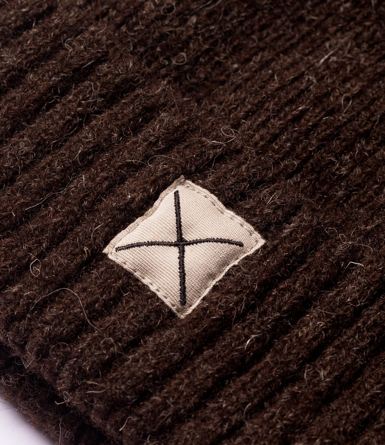 Close-up of the Shetland Cap of Courage by Best Made Co: brown undyed Shetland wool knit with a small beige patch at center, featuring a black stitched X.