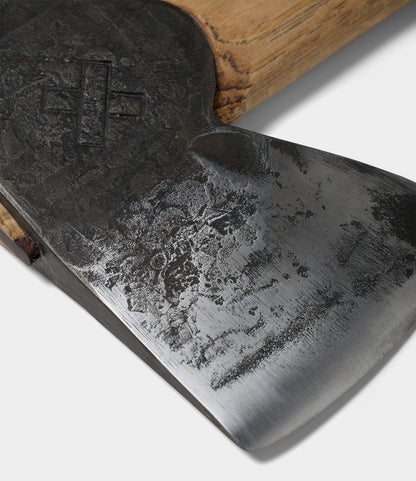 Close-up of The Phantom axe blade by Best Made Co., featuring a weathered Rockaway pattern, cross symbol near the wooden handle, and hand-forged high-carbon steel, photographed on a white background.
