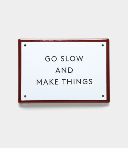 The “Go Slow” Enamel Steel Sign by Best Made Co. features black uppercase text on white enamel with a red border—durable wall decor for any space.