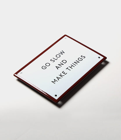 The “Go Slow” Enamel Steel Sign by Best Made Co. is a white, rectangular sign with a red border and black lettering—ideal as durable wall decor.