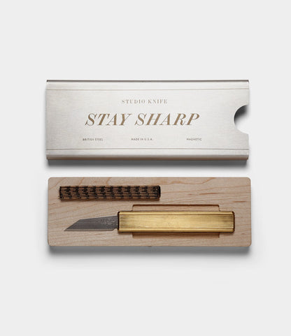 The Best Made Co. Studio Knife features a brass handle, comes in a wooden case with a spare workshop blade, and includes a metal lid engraved with “STUDIO KNIFE STAY SHARP.”.
