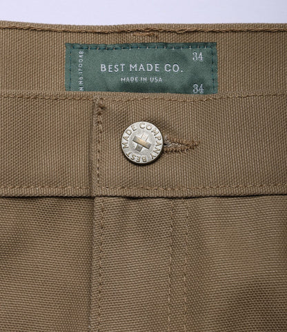 Close-up of Standard 5-Pocket Pant Tan by Best Made Co., highlighting a metal button engraved with the brand and a green waist label reading "Best Made Co., Made in USA, 34.