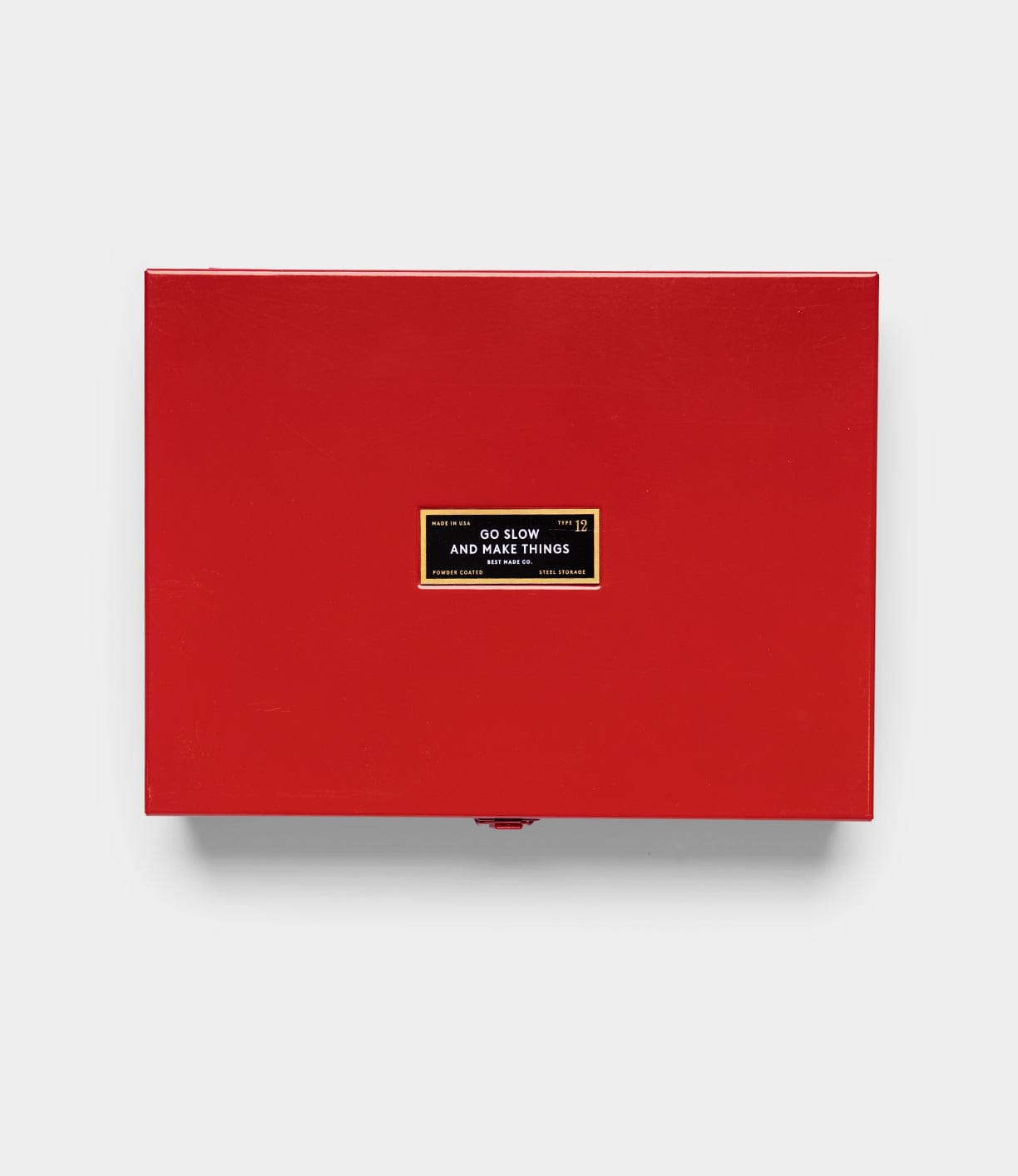 The Best Made Co Type 12 Strongbox, Go Slow Edition, is a red rectangular steel storage box featuring a central black and gold label with the words "GO SLOW AND GO SLOWINGS MAKE THINGS," shown against a plain light gray background.