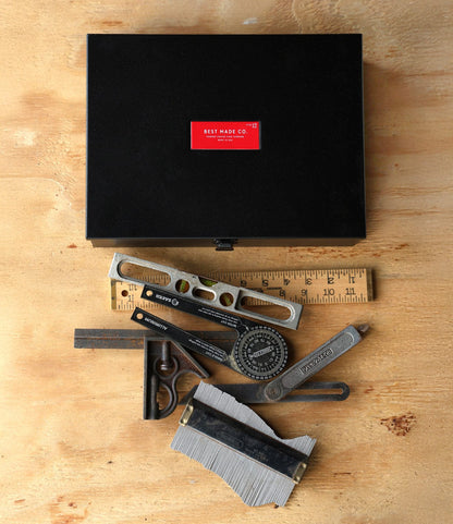 The Best Made Co. Type 12 Strongbox - Matte Black sits on a wooden surface, surrounded by measuring tools—a ruler, level, protractor, caliper, and gauge—offering secure storage for your essentials.