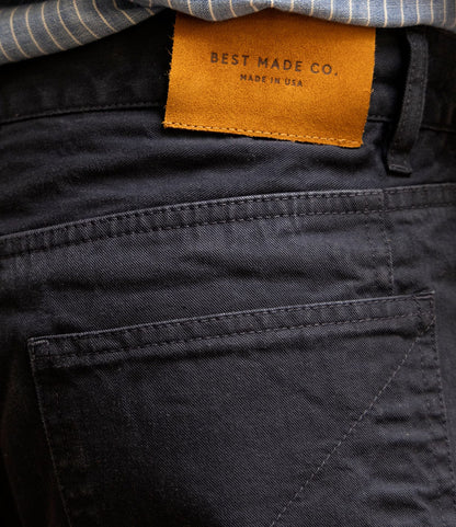 A close-up of the back pocket on Field Pant Special Edition Navy by Best Made Co., showing a brown leather brand patch. A blue-and-white striped shirt is partially visible above the waistband.