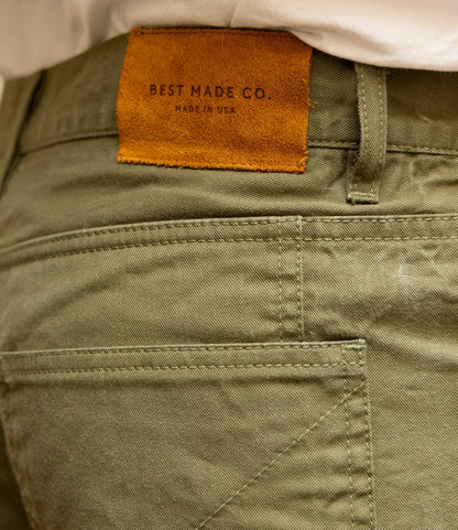 Close-up of the back pocket and waistband of the Field Pant Special Edition Olive Drab by Best Made Co., featuring a brown leather patch stamped with the brand's name. A white shirt is partially visible at the top.