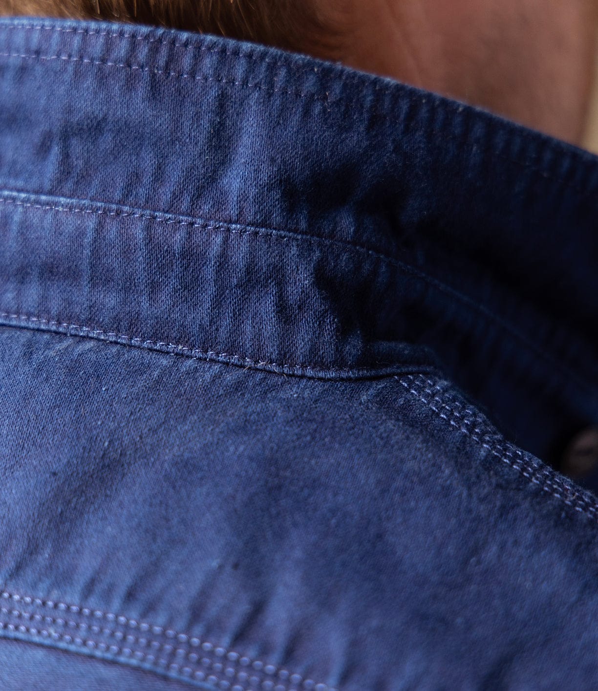 Close-up of the back collar and shoulder of the Best Made Co Indigo Moleskin Work Shirt, highlighting its detailed stitching and rich texture, with part of a person's neck and hair in the background.
