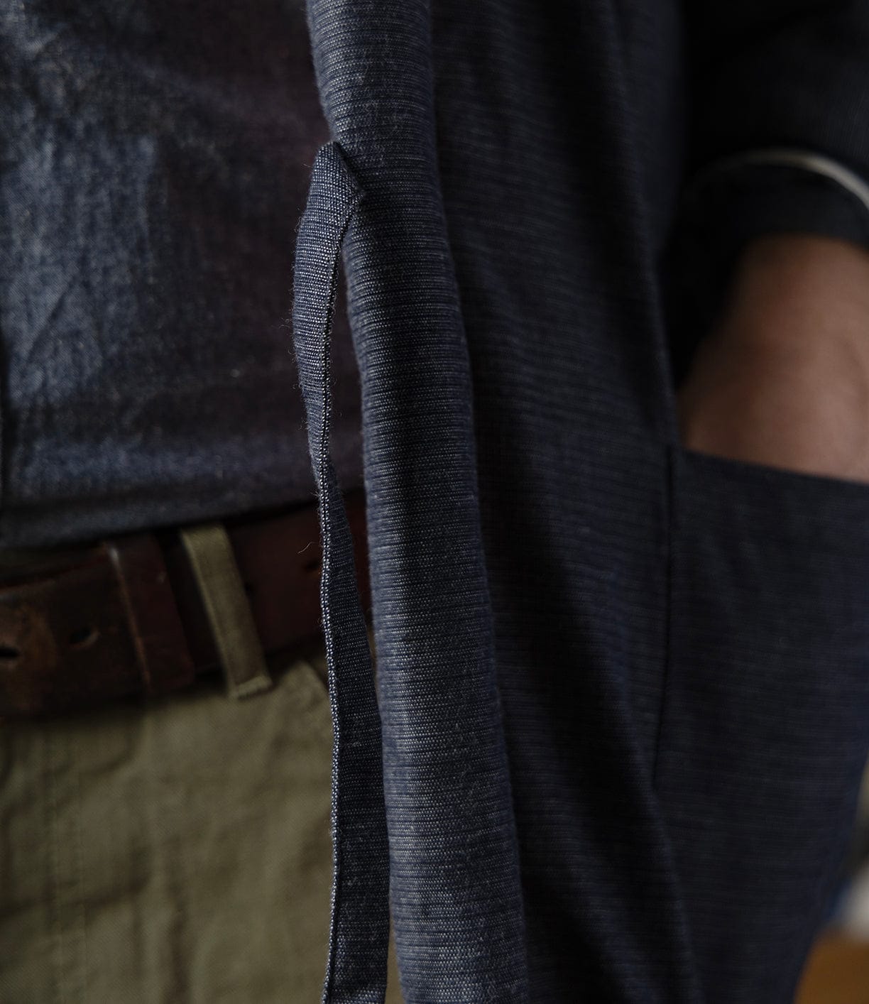 Close-up of a person wearing the Best Made Co. Quilted Hanten Jacket with a belt tie, paired with olive green pants and a brown belt. Their hand is partially visible, resting in the jacket pocket.