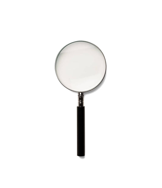 A Best Made Co. Magnifying Glass and a transparent ruler are placed on a wooden surface near a brass door latch.