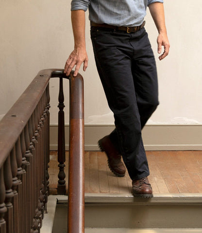 A person wears a blue shirt and Best Made Co. Field Pant Special Edition Navy, paired with brown shoes, while walking down wooden stairs holding the railing. The person's head is not visible in the image.