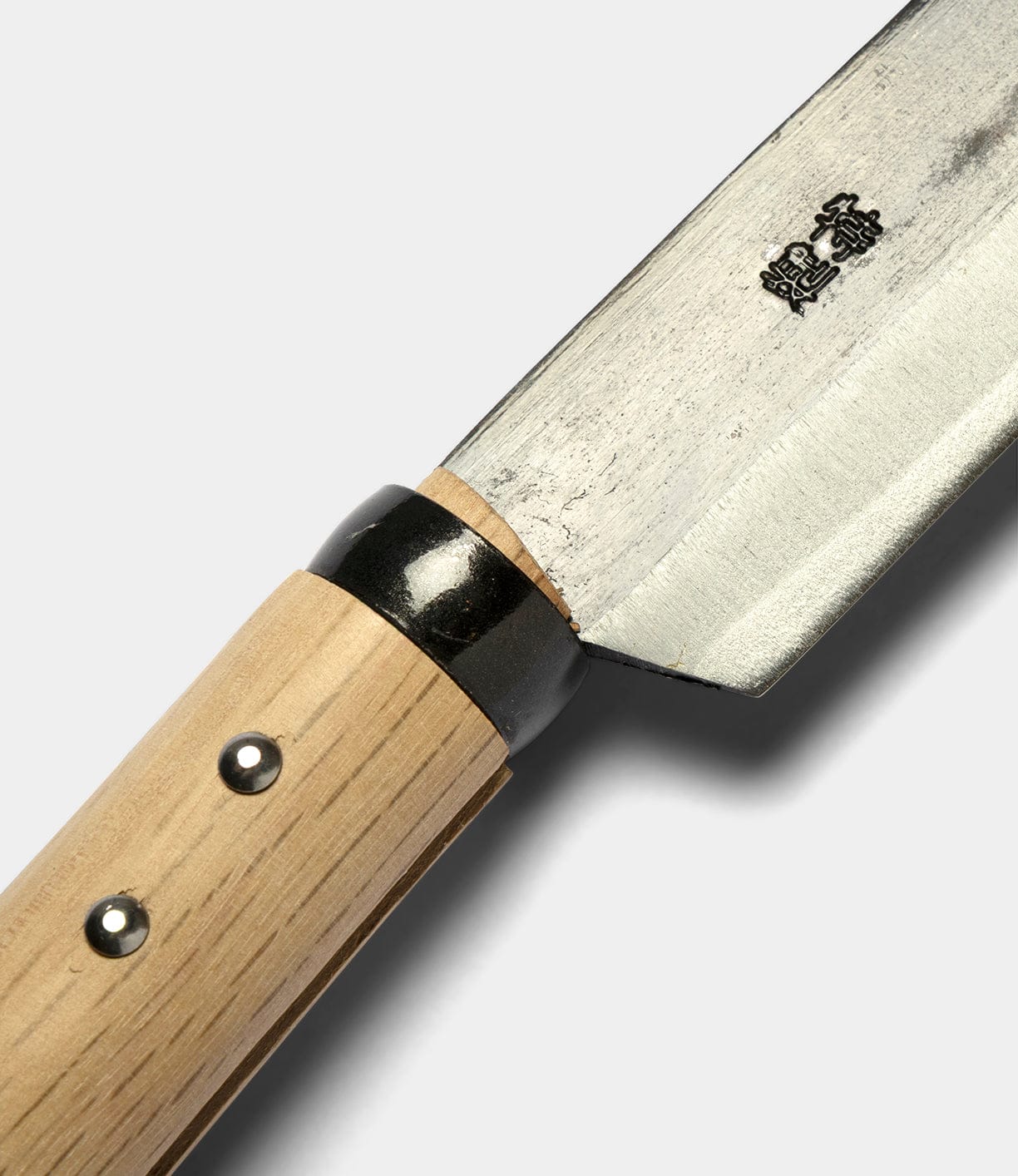 Close-up of the Japanese Hatchet by Best Made Co, featuring a wooden handle, metal rivets, and a steel blade etched with Japanese characters against a plain, light background.