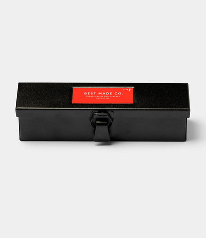 The Best Made Co. Type P Strongbox in matte black, a rectangular metal pencil storage box with a latch and a red label on top, is shown against a plain light gray background.