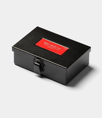 The Best Made Co. Type 6 Strongbox in matte black is a durable rectangular steel box with a latch and a red label on top stating BEST MADE CO., shown against a plain light background.