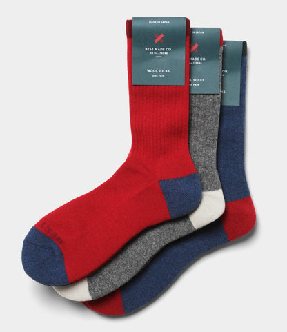 Three pairs of Best Made Co. Japanese Wool Socks—crew-length in red, gray, and blue with contrasting toe and heel—are stacked with labels at the cuffs, offering perfect cold-weather warmth.