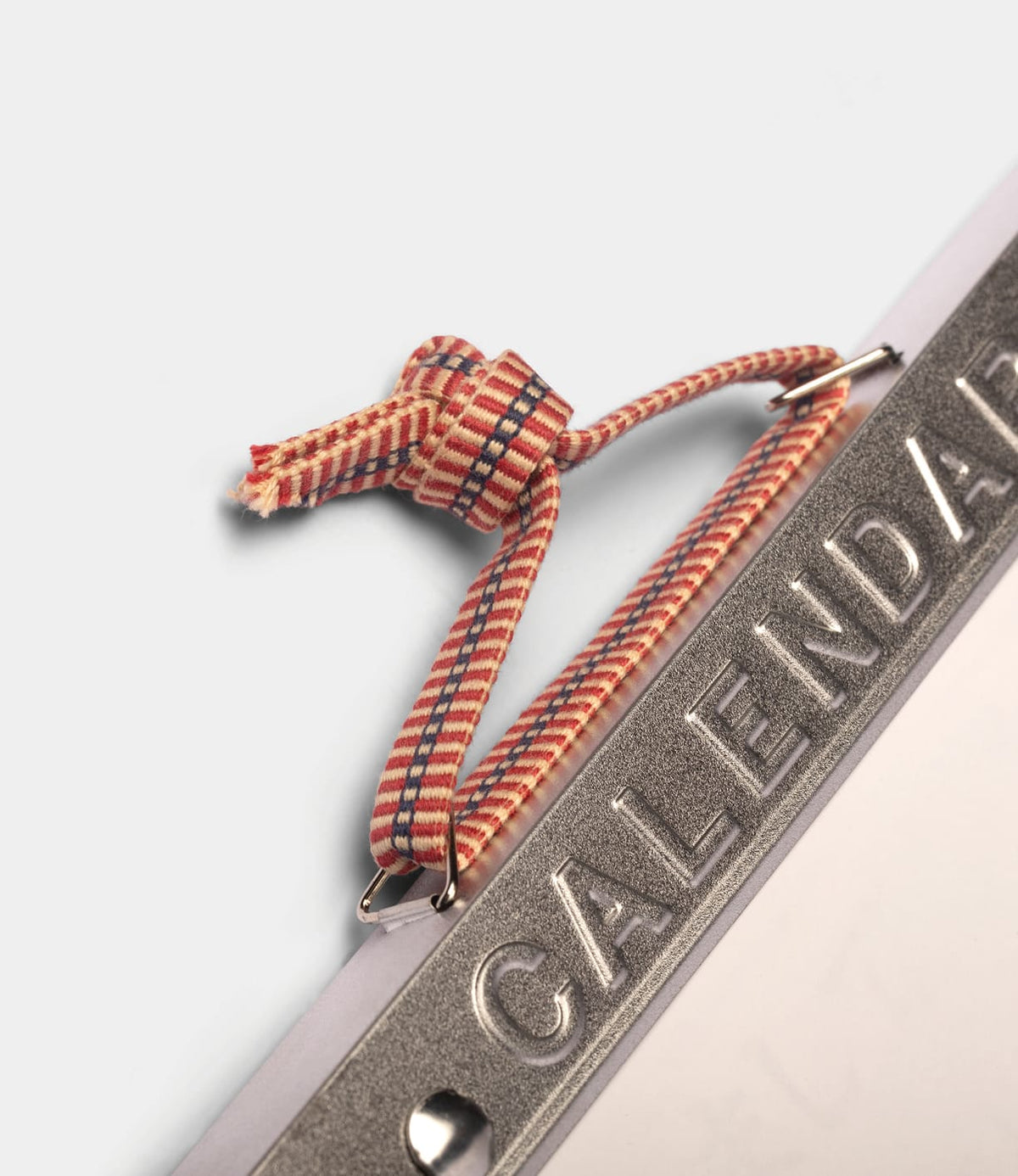 A metal top from a Himekuri Calendar 2027, featuring a red and blue patterned fabric loop knotted at the top.