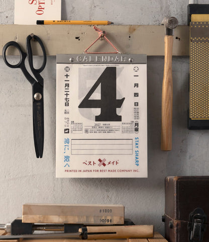 A wall-mounted Himekuri Calendar 2027 showing the date as the number four, hanging above a sharpening stone and various workshop tools.