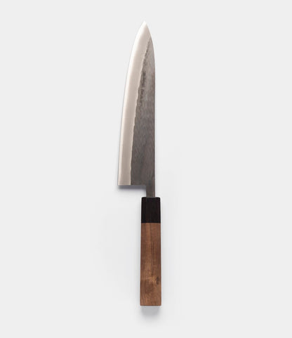 A vertical studio shot of the Aogami Gyuto Knife by Best Made Co. against a plain white background. This gyuto knife showcases a polished, dark-textured blade—expertly forged from Blue Paper Steel No. 2—and features a two-toned wooden handle.