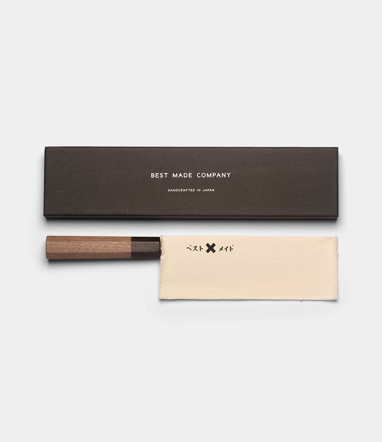 Certainly! Here’s a rewritten version of the sentence using your product data: The Aogami Santoku Knife by Best Made Co. features a wooden handle, includes a protective cream-colored fabric sleeve, and comes packaged in a dark rectangular storage box labeled with the Best Made Co. name. Expertly crafted in Japan, this versatile kitchen knife is designed for precision in every culinary task.