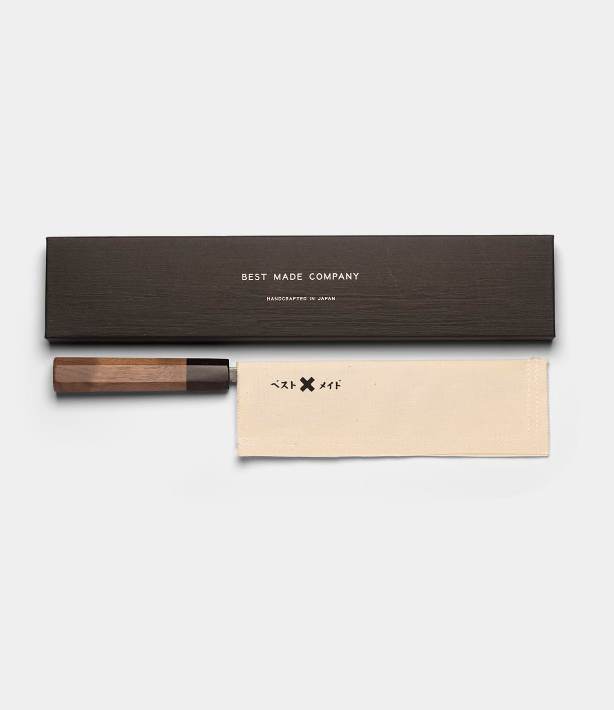 The Aogami Gyuto Knife by Best Made Co. features a wooden handle and a blade forged from Blue Paper Steel No. 2, presented in a cream cloth sheath decorated with symbols and enclosed within a black rectangular box bearing the Best Made Co. name.